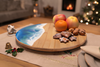 Drehteller aus Bambus mit abgerundeten Kanten mit Meereswellen-Design aus Epoxidharz in blau und weiß, auf dem Drehteller sind 2 Äpfel, 1 Mandarinen, Nüsse und weihnachtliche Kekse, der Drehteller steht auf einem Tisch mit beiger Tischdecke und weihnachtl