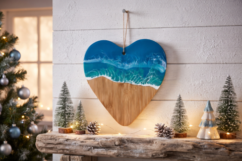 Herz aus Bambus mit Meereseffekt, aufgehängt an weißer Wand mit Weihnachtsdeko auf Holzbrett unterhalb des Herzes. Im Hintergrund ist ein Weihnachtsbaum und ein Fenster zu sehen