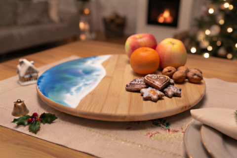 Drehteller aus Bambus mit abgerundeten Kanten mit Meereswellen-Design aus Epoxidharz in blau und weiß, auf dem Drehteller sind 2 Äpfel, 1 Mandarinen, Nüsse und weihnachtliche Kekse, der Drehteller steht auf einem Tisch mit beiger Tischdecke und weihnachtl