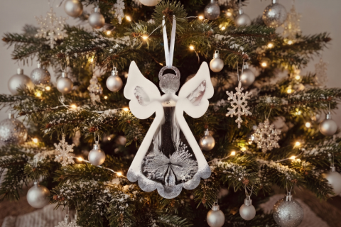 Engel aus Epoxidharz in weiß und silber mit weißem Satinband aufgehängt an einem Tannenzweig eines Weihnachtsbaumes, der mit silbernen Kugeln und Sternen dekoriert ist