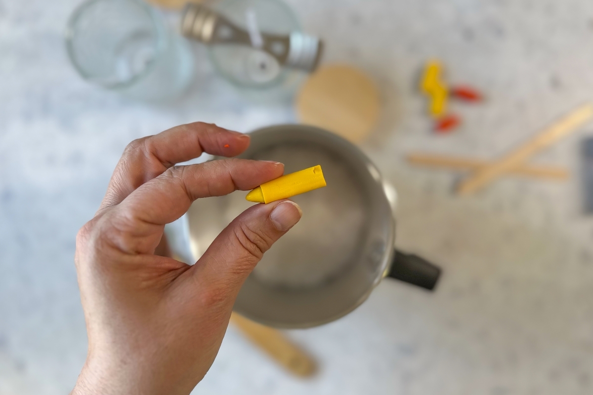 Ein Wachsmalstift wird in der Hand &uuml;ber einen Topf gehalten.