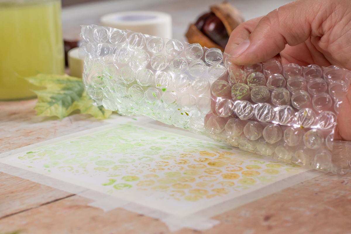 Luftpolsterfolie mit Farbe drauf wird auf ein Blatt Papier gedrückt.