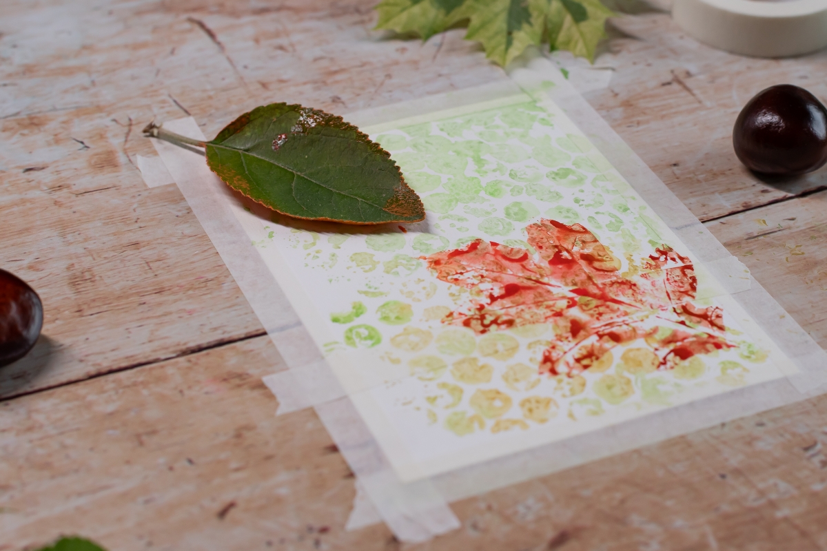 Farbige Adrücke von einem Pflanzenblatt auf einem Blatt Papier.