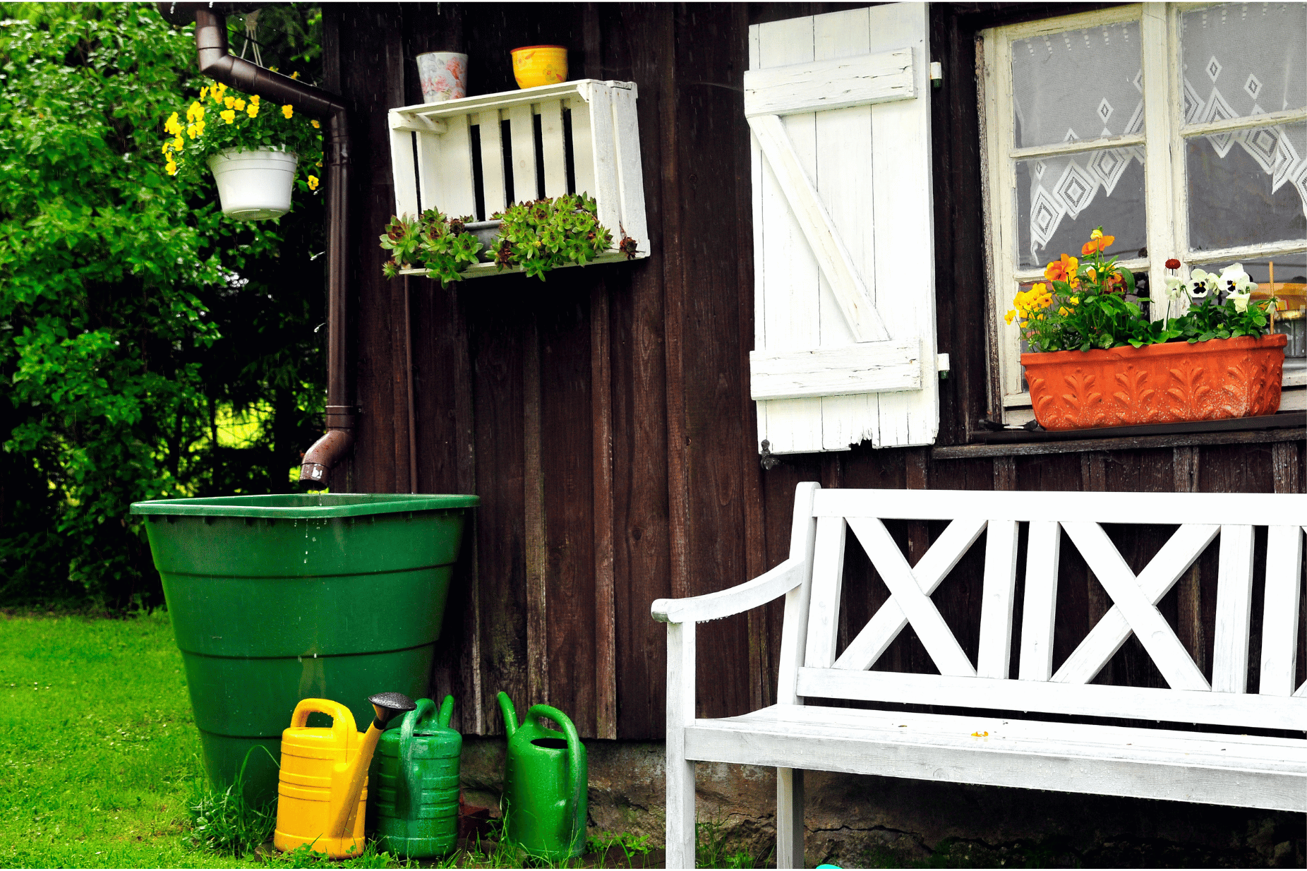 Ein Garten mit einem Gartenhäuschen, einer Sitzbank, einer Regentonne und drei Gießkannen. 