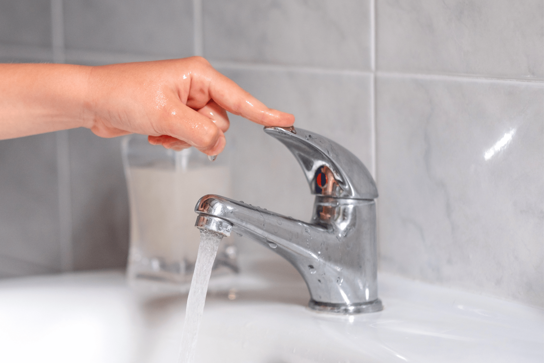 Kinderhand  über einem Waschbecken und macht den Wasserhahn aus. 
