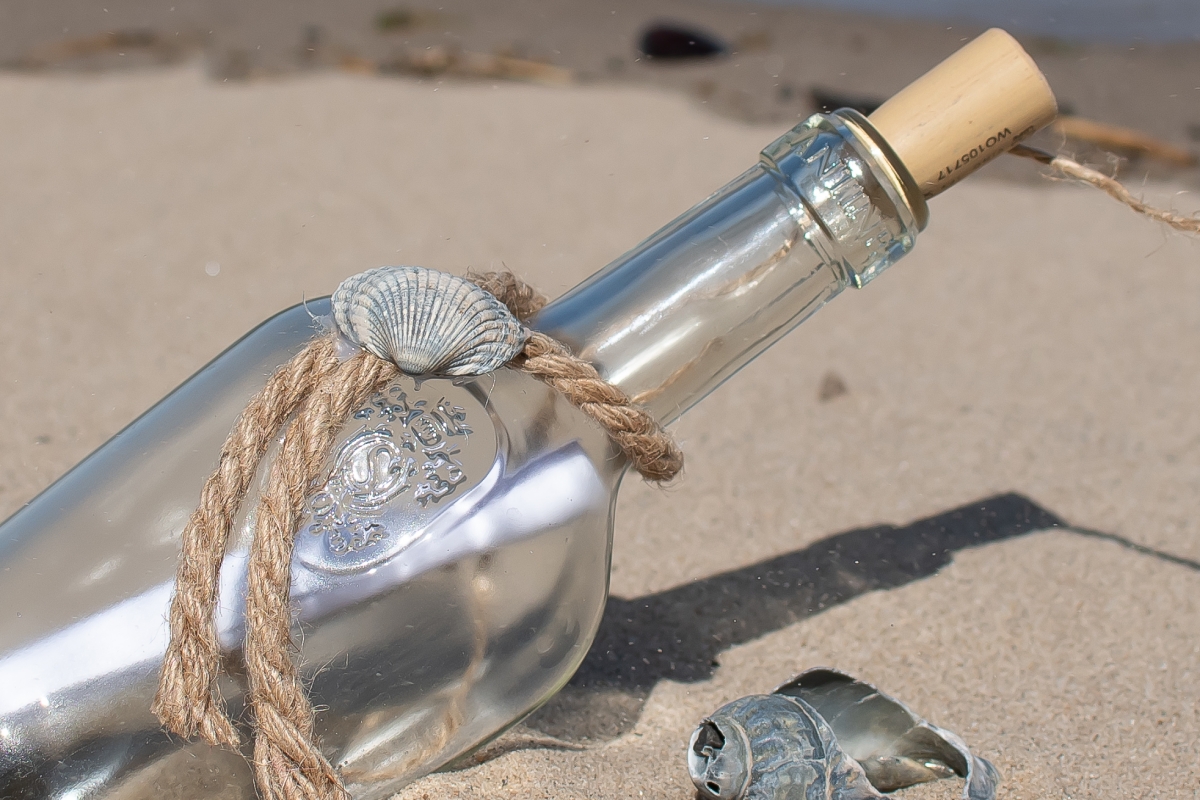Eine Flasche mit einem Zettel darin liegt im Sand. 