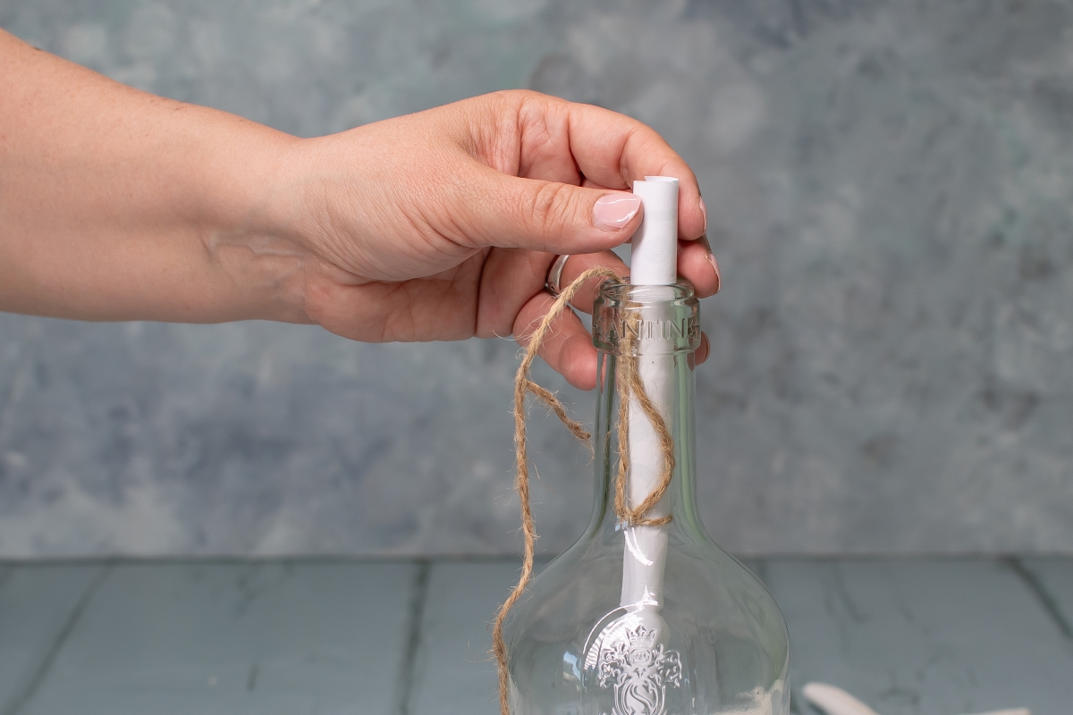 Ein zusammengerolltes Papier wird in einen Flaschenhals gesteckt. 
