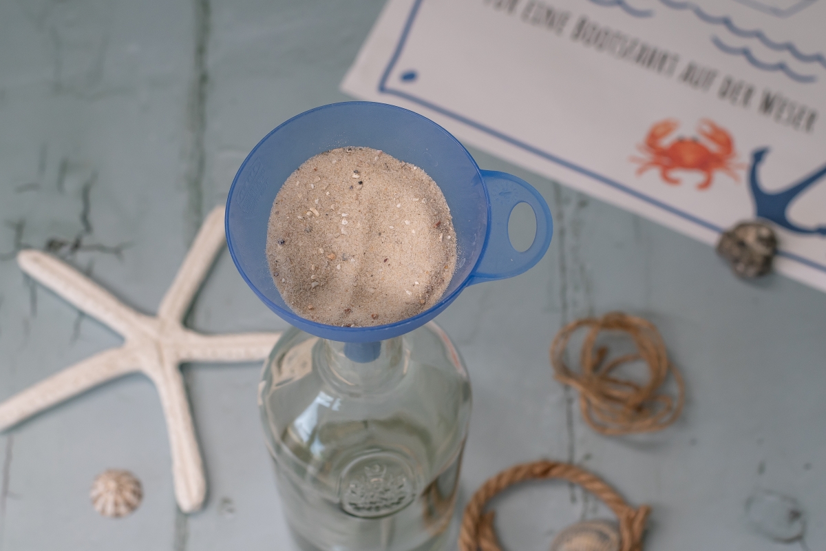 Sand wird mit einem Trichter in eine Flasche gefüllt. 