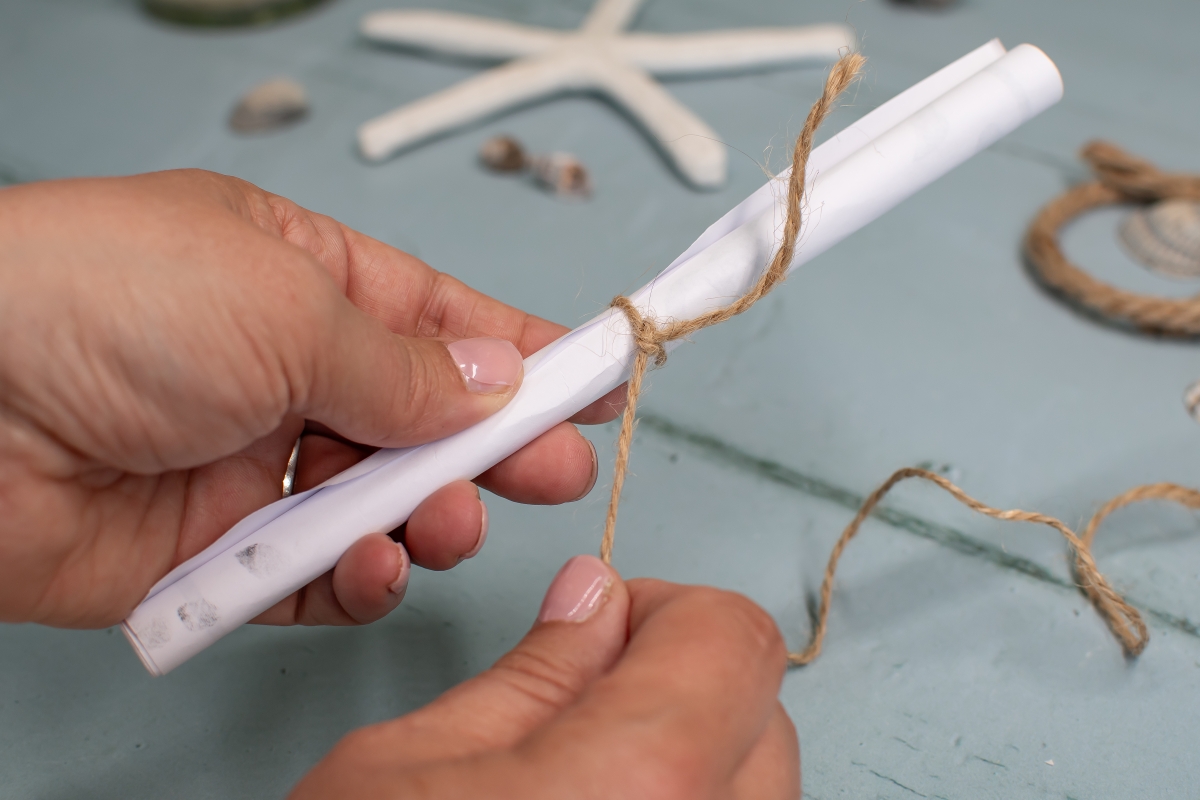 Ein zusammengerolltes Papier wird mit Juteband zusammengeknotet. 